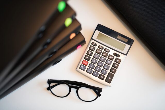 Dosare ordonate și un calculator pe un birou, folosite pentru evidența cheltuielilor unui proiect